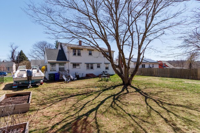 rear view of house featuring a yard, fence, a garden, and a chimney