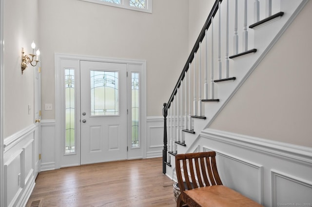 foyer entrance with stairway, a wainscoted wall, a decorative wall, and wood finished floors