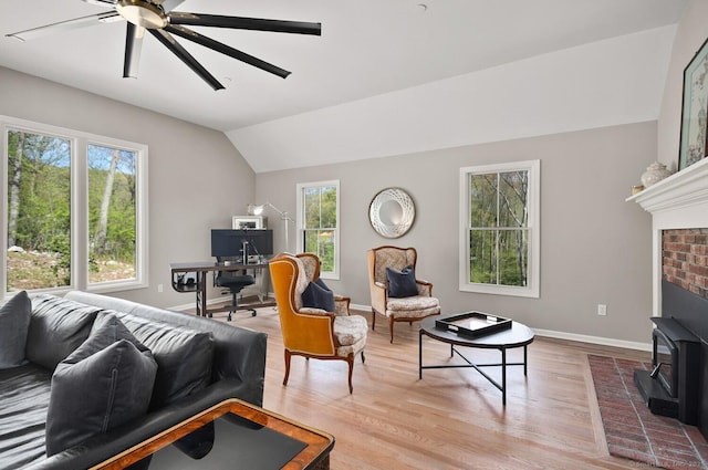 living room featuring ceiling fan, vaulted ceiling, a wood stove, wood finished floors, and baseboards
