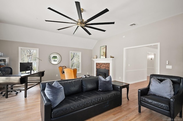 living room featuring a ceiling fan, visible vents, a fireplace, light wood finished floors, and lofted ceiling
