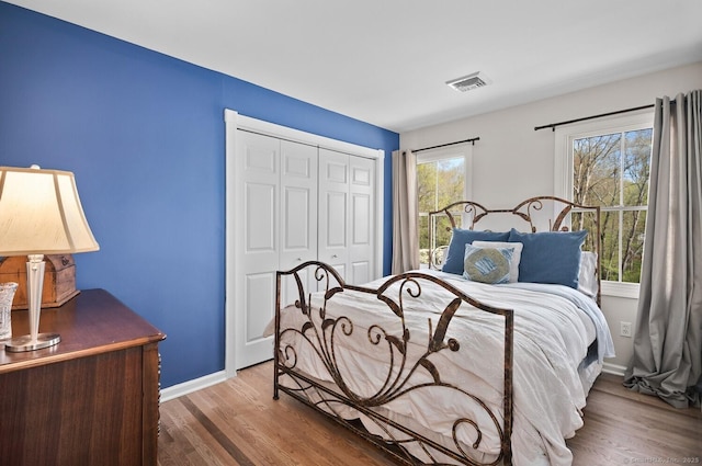 bedroom with baseboards, a closet, wood finished floors, and visible vents