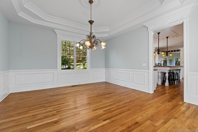 unfurnished dining area with light wood-style floors, a chandelier, and a raised ceiling