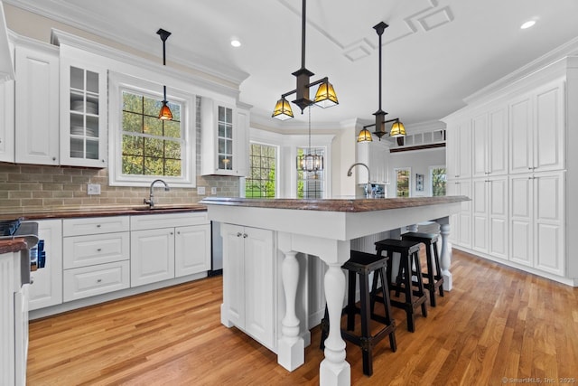 kitchen featuring a sink, light wood finished floors, crown molding, and white cabinets
