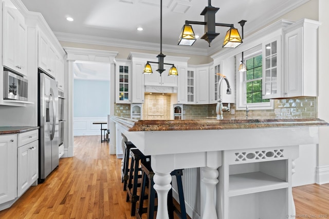 kitchen with a kitchen bar, a sink, stainless steel appliances, white cabinets, and light wood-style floors