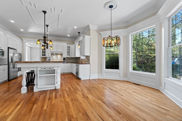kitchen with ornamental molding, a notable chandelier, open shelves, and appliances with stainless steel finishes