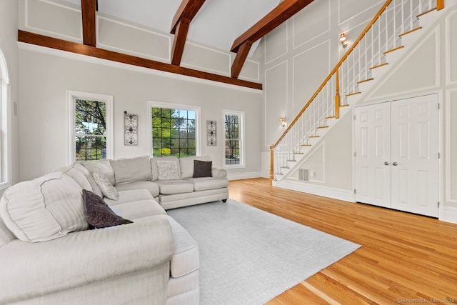 living area with light wood-style floors, beamed ceiling, and stairs