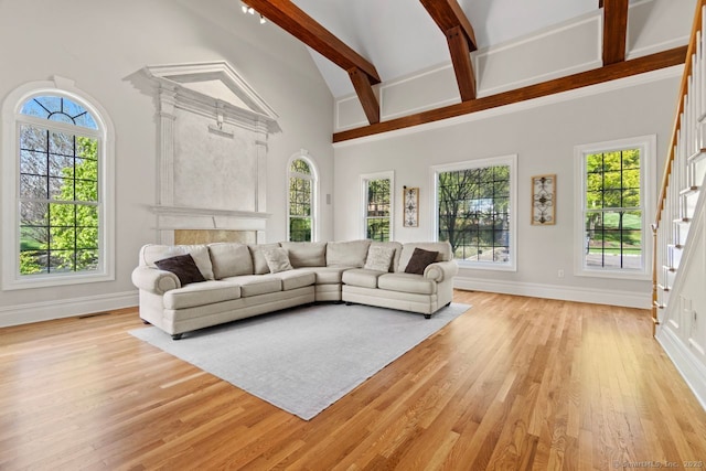 living room featuring light wood-style flooring, a healthy amount of sunlight, baseboards, beamed ceiling, and stairs