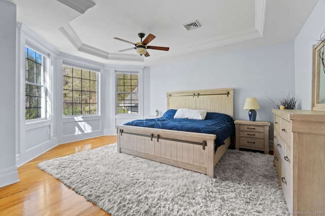 bedroom with multiple windows, visible vents, wood finished floors, and a raised ceiling
