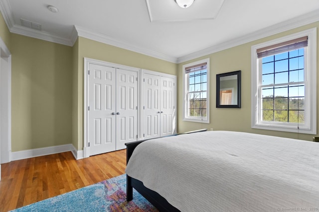 bedroom featuring wood finished floors, visible vents, two closets, crown molding, and baseboards