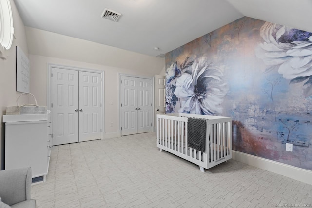 bedroom with two closets, lofted ceiling, baseboards, and visible vents