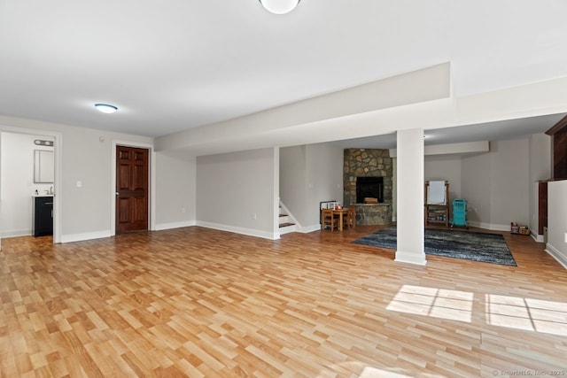 finished basement featuring baseboards, a stone fireplace, light wood-style floors, and stairway