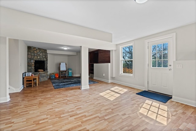 interior space featuring light wood finished floors, baseboards, and a stone fireplace