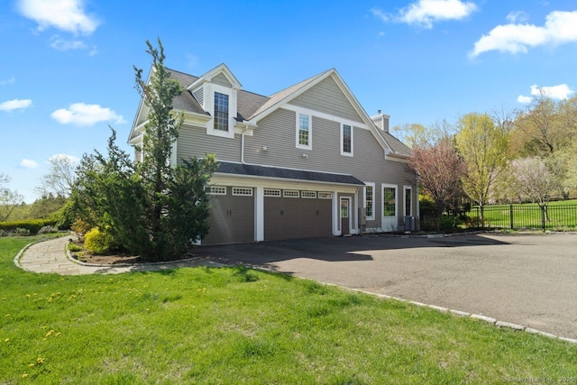 view of side of home with a garage, a chimney, a lawn, fence, and driveway