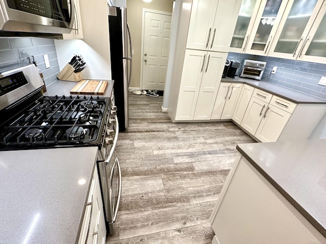 103D Wendover Dr Unit D, Monroe, CT 06468 - kitchen featuring appliances with stainless steel finishes, light wood-style floors, decorative backsplash, and glass insert cabinets