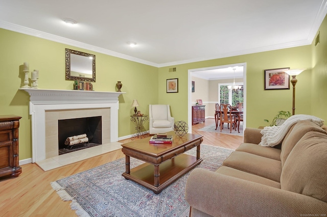 living room with ornamental molding, wood finished floors, a chandelier, baseboards, and a tiled fireplace