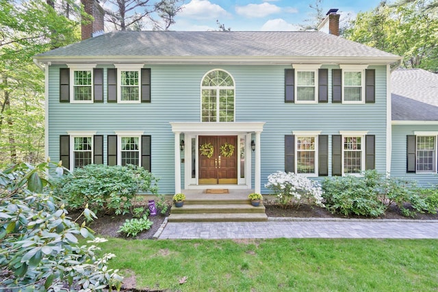 colonial home featuring a chimney, a shingled roof, and a front yard
