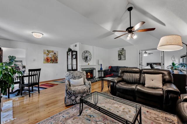 living area featuring a ceiling fan, visible vents, a fireplace, vaulted ceiling, and light wood-type flooring