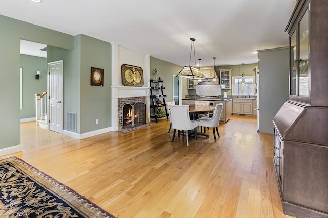 dining area featuring a fireplace, baseboards, visible vents, and light wood-style floors