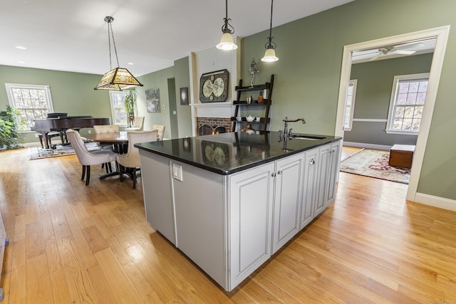kitchen with a sink, light wood-style flooring, hanging light fixtures, and dark countertops