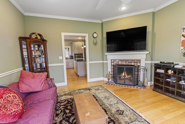 living room with ornamental molding, a brick fireplace, baseboards, light wood-type flooring, and a ceiling fan