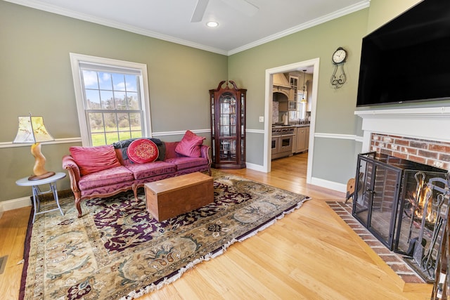living room with crown molding, a fireplace, a ceiling fan, baseboards, and wood finished floors