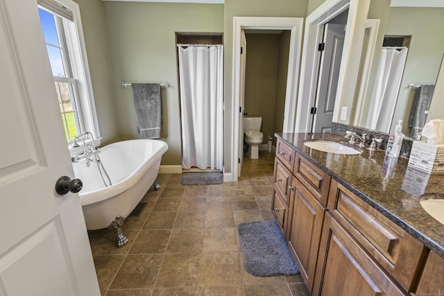bathroom with a sink, double vanity, toilet, baseboards, and a soaking tub