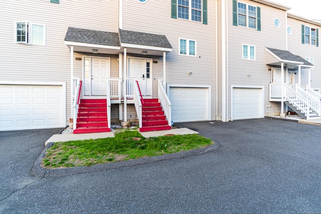 multi unit property featuring driveway, roof with shingles, and a garage