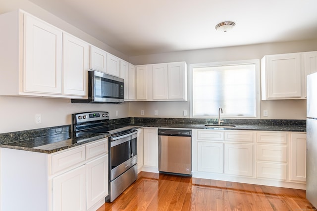 kitchen with a sink, appliances with stainless steel finishes, dark stone countertops, and white cabinetry