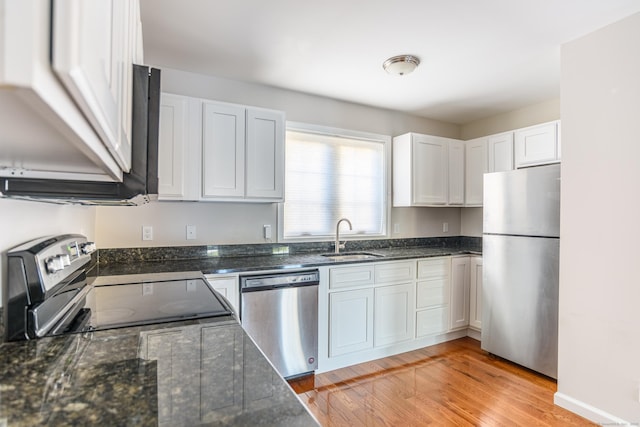 kitchen featuring a sink, light wood-style flooring, dark stone counters, stainless steel appliances, and white cabinetry