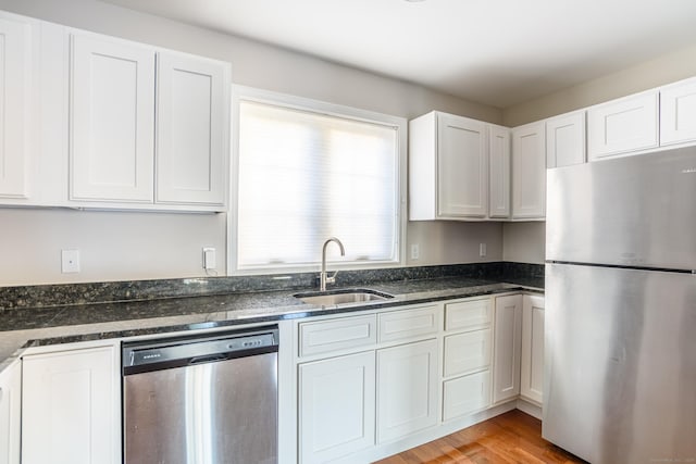 kitchen featuring a sink, appliances with stainless steel finishes, white cabinets, and dark stone counters