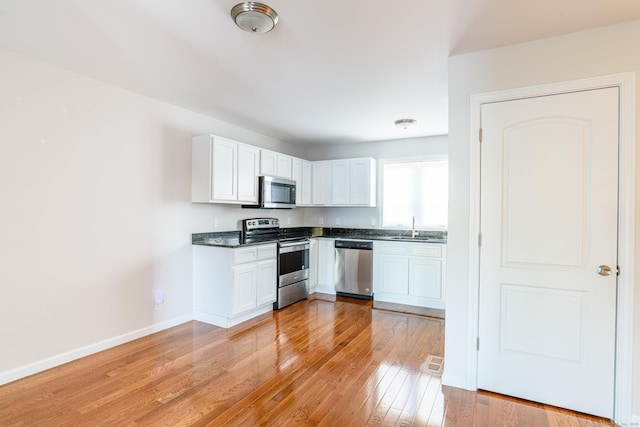 kitchen with dark countertops, baseboards, light wood-type flooring, a sink, and appliances with stainless steel finishes