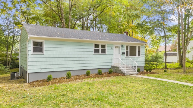 ranch-style home with central air condition unit, roof with shingles, and a front yard