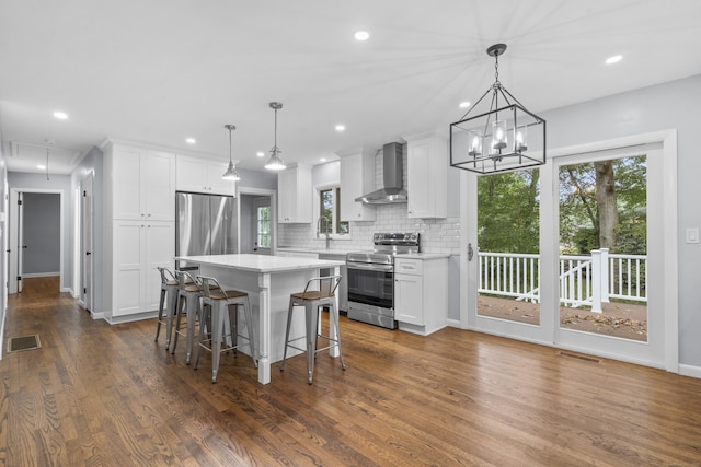 kitchen featuring wall chimney range hood, stainless steel appliances, white cabinetry, tasteful backsplash, and visible vents