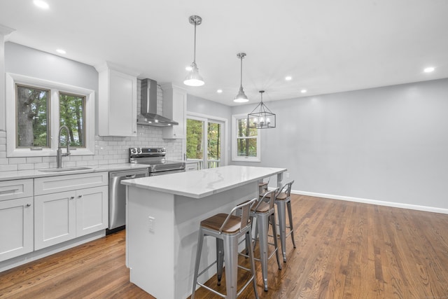 kitchen featuring a kitchen island, wall chimney range hood, white cabinets, a sink, and appliances with stainless steel finishes