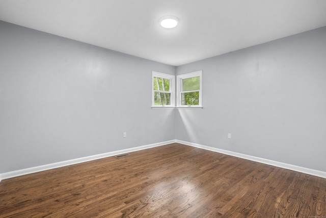 unfurnished room with dark wood-style flooring, baseboards, and visible vents