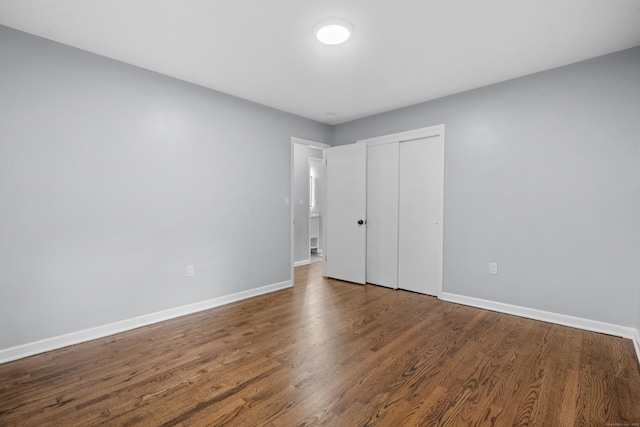 unfurnished bedroom featuring baseboards, dark wood finished floors, and a closet