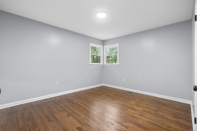 unfurnished room featuring baseboards, dark wood-type flooring, and visible vents
