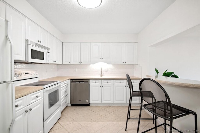 kitchen with a sink, white appliances, tasteful backsplash, white cabinetry, and light countertops