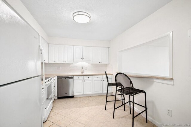 kitchen featuring a textured ceiling, white appliances, decorative backsplash, light countertops, and white cabinets
