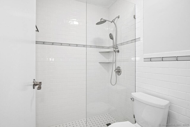 bathroom with tile walls, toilet, and a tile shower