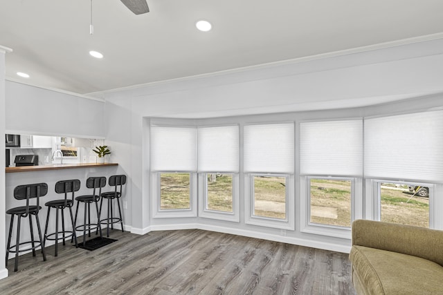 interior space featuring crown molding, a breakfast bar, a wealth of natural light, and wood finished floors