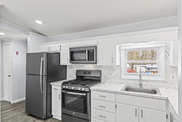 kitchen with backsplash, a sink, ornamental molding, stainless steel appliances, and white cabinetry