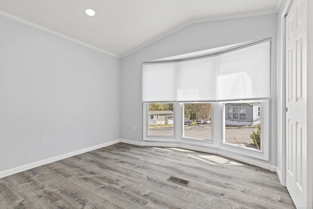 empty room featuring crown molding, baseboards, wood finished floors, lofted ceiling, and visible vents