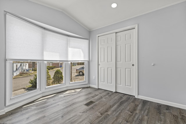 unfurnished bedroom with visible vents, wood finished floors, a closet, lofted ceiling, and ornamental molding
