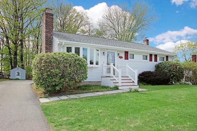 single story home featuring an outbuilding, a chimney, a shed, and a front yard