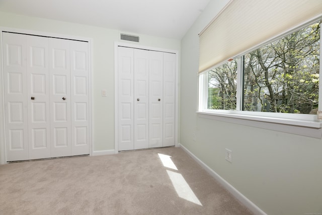 unfurnished bedroom featuring two closets, baseboards, visible vents, and carpet floors