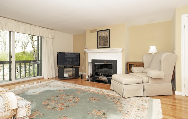 living room featuring visible vents, a fireplace with flush hearth, baseboards, and wood finished floors