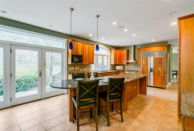 32 Village Dr, East Lyme, CT 06333 - kitchen with wall chimney range hood, built in appliances, brown cabinets, tasteful backsplash, and an island with sink