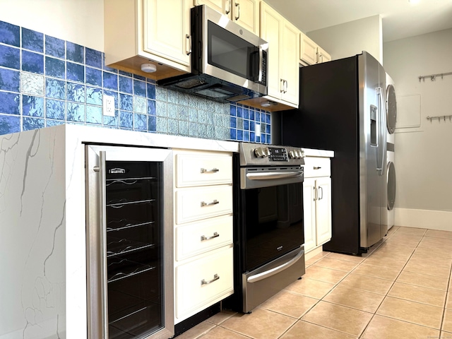 kitchen with beverage cooler, appliances with stainless steel finishes, stacked washer / drying machine, light tile patterned flooring, and decorative backsplash