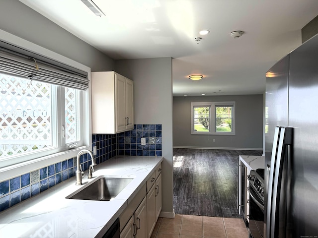 kitchen featuring appliances with stainless steel finishes, a sink, light stone counters, baseboards, and open floor plan
